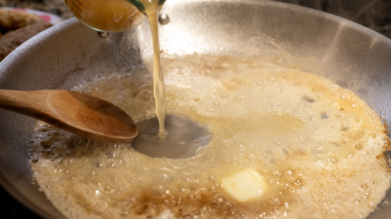 close up of a pan cooking a sauce on the stove and a hand pouring in broth