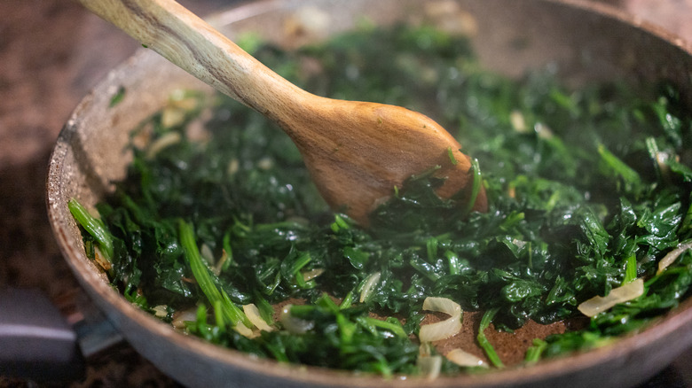 close up of greens being sauteed in a pan with a wooden spoon