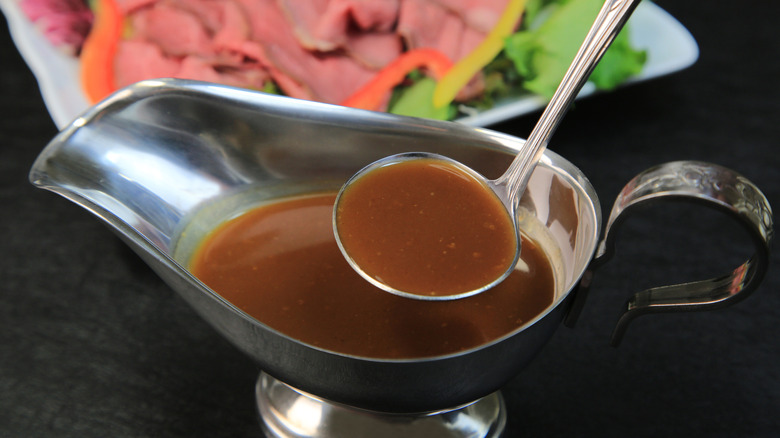 gravy boat filled with au jus dipping sauce with a ladel in front of sliced meat