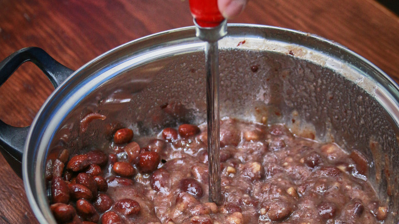 Mashing beans in a pot with a small hand mixing wand