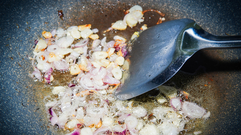 Spatula stirring garlic and onions sautéing in a pan