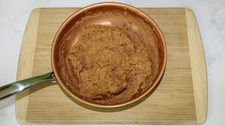 Pan of refried beans on a wooden cutting board