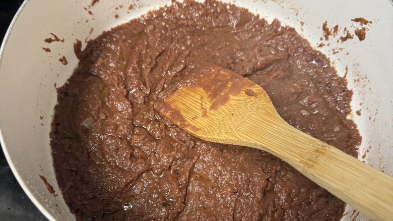 Refried beans cooking in a pan with a wooden spoon