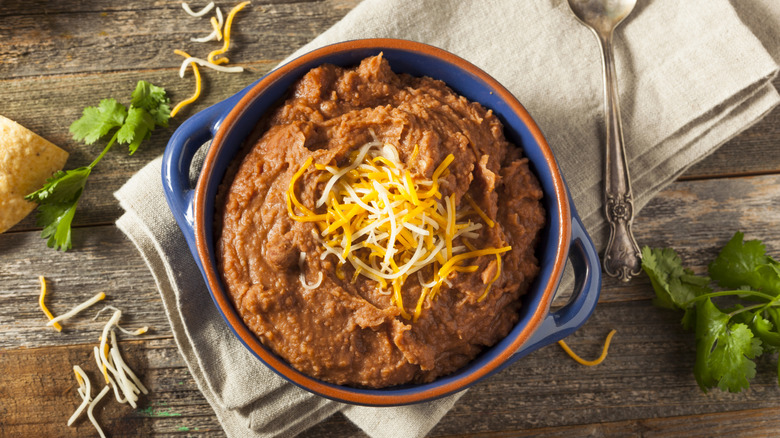 Overhead view of a bowl of homemade refried beans sprinkled with shredded cheese