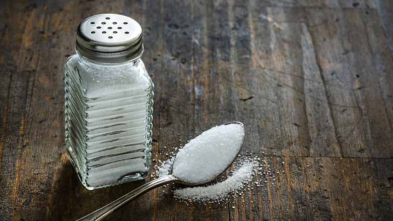 Glass shaker of salt next a spoonful of salt
