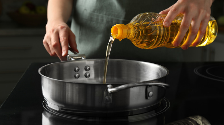 Hands pouring vegetable oil into a frying pan