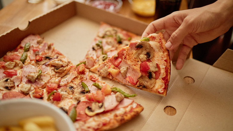 A hand takes a slice of pizza out of a pizza box.