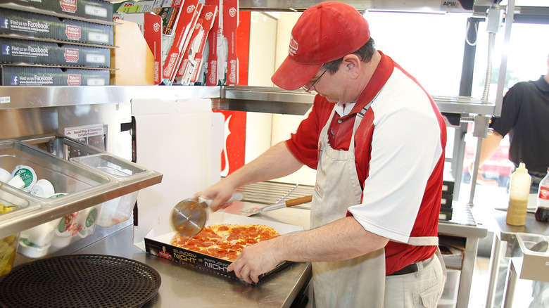 A Papa John's employee slices a pizza inside a to-go box.