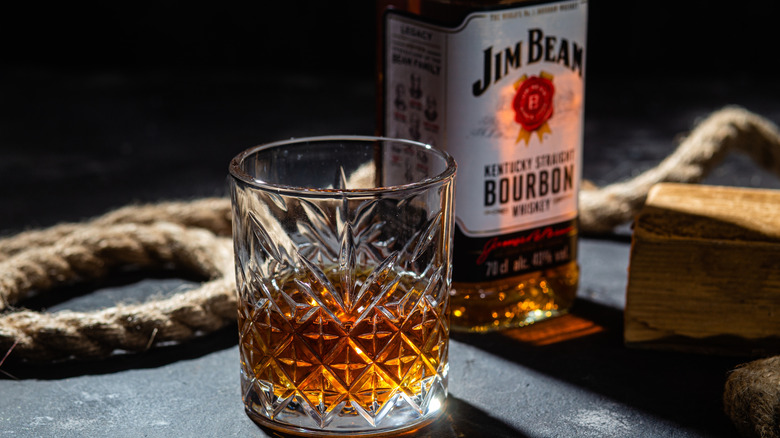 A bottle of Jim Beam bourbon whiskey sits behind a glass of bourbon.