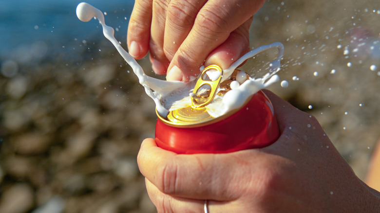 Foam spraying out as a woman's hands opened a can of beer