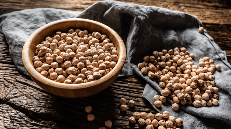Chickpeas in a wooden bowl and scattered across a cltoh on a wooden table