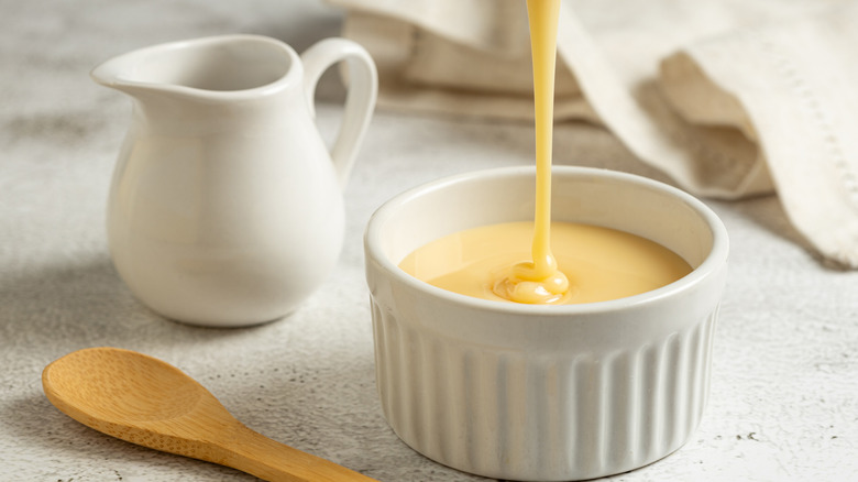 Condensed milk poured into a ramekin beside a pitcher and wooden spoon