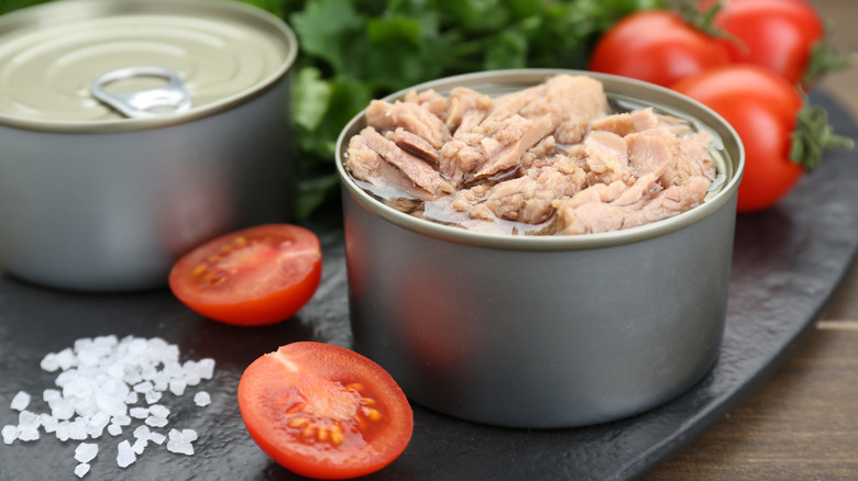 Cans of tuna on a serving board with tomatoes salt and greens