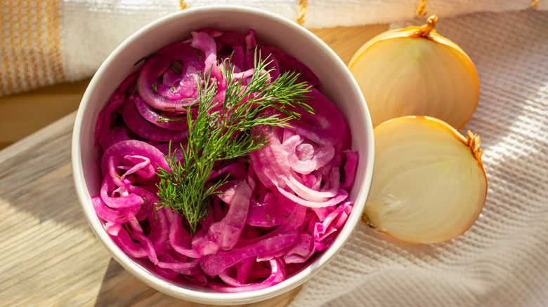 A bowl of pickled red onions next to a halved yellow onion