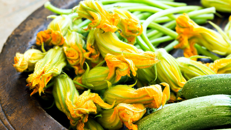Squash blossoms next to zucchini on a plate