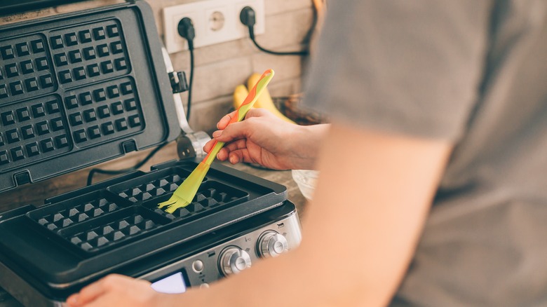 Man greasing a waffle iron with brush