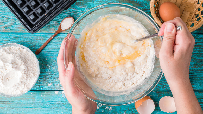 Hand stirring bowl of batter on blue background