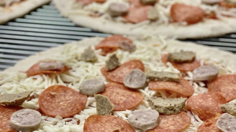 Uncooked pizza topped with three meats and shredded mozzarella