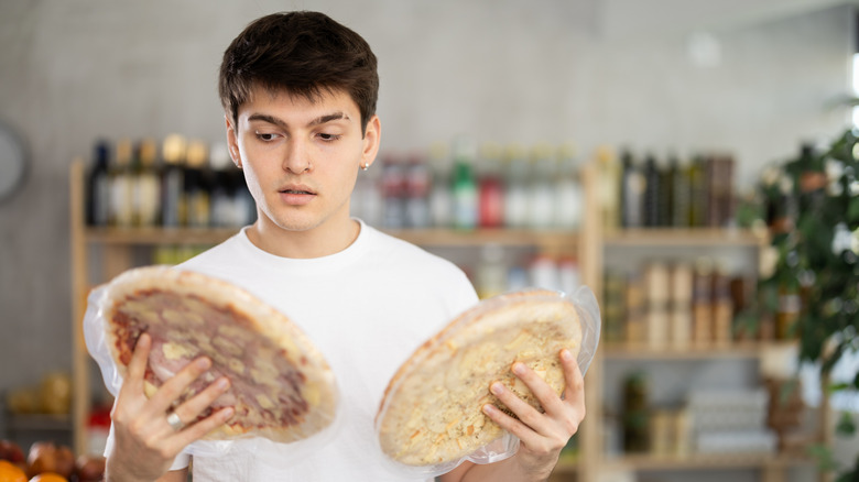 Guy looking at two frozen pizzas
