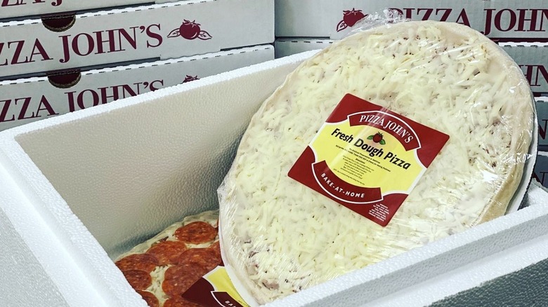Sealed frozen pizza jutting out of a styrofoam container in front of a stack of pizza boxes