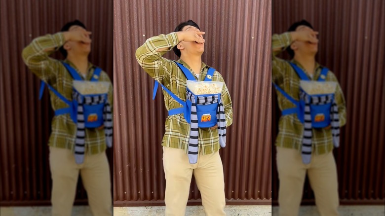 A moviegoer wears and eats popcorn from a "Despicable Me 4" baby carrier popcorn holder