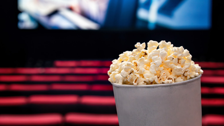 A popcorn bucket with a blurred movie theater screen and cinema seats in the background