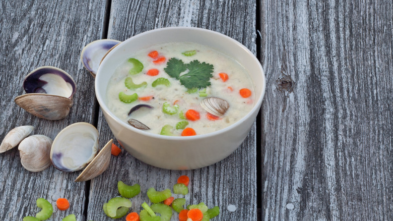 Bowl of clam chowder with celery on wooden background