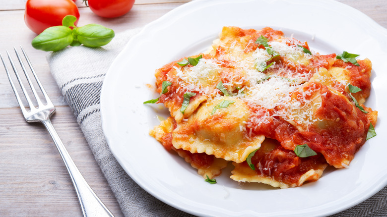 Basil, cheese, and sauce covered dish of ravioli in a white plate served atop a napkin