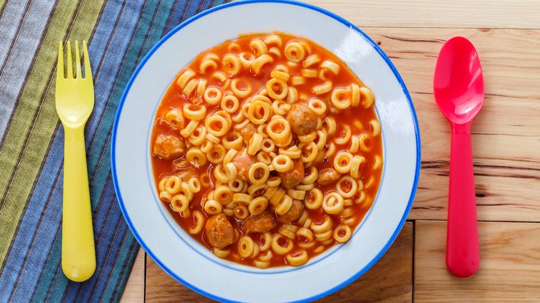 Bowl of spaghetti rings with meatballs in sauce with colorful utensils on a wooden table