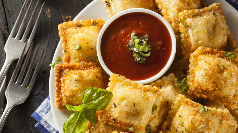 Plate of fried ravioli with a marinara dipping sauce on a dark wooden table with forks