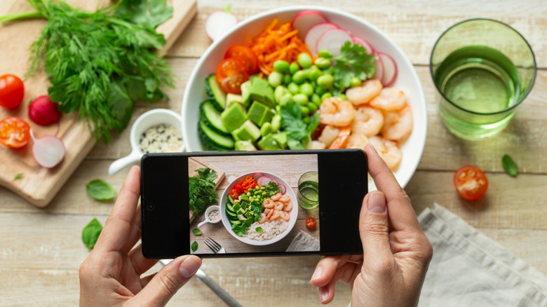 A woman's hands taking a photo of a lunch bowl