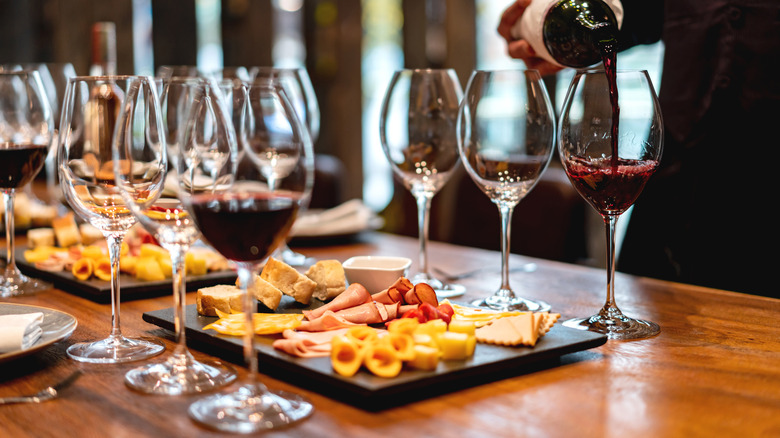 a waiter pouring red wine into a glass next to charcuterie boards