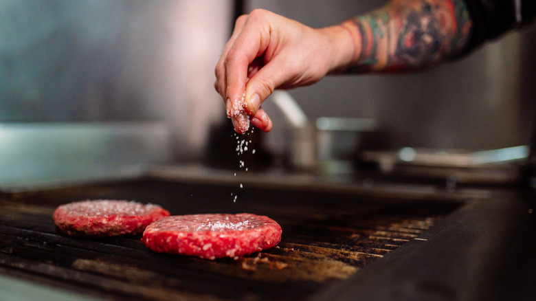 Hand adding salt to raw burger