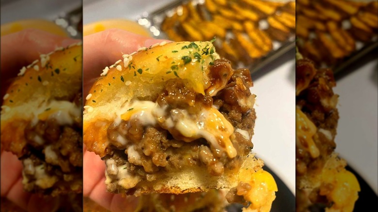 A hand holds a bacon cheeseburger slider.
