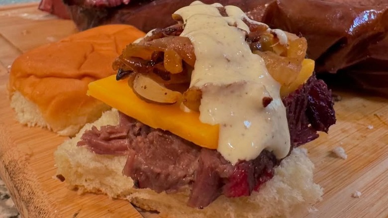 A brisket slider sits on a wooden cutting board.