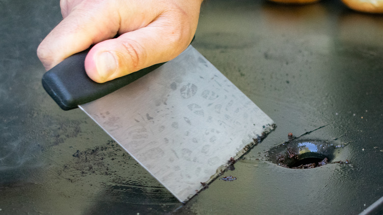 person scraping clean griddle plate