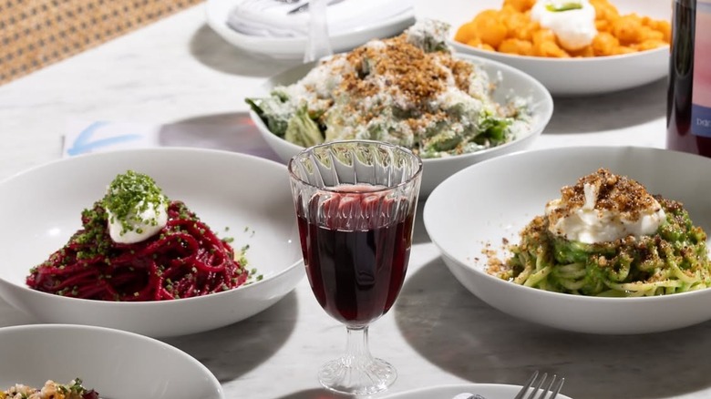 a glass of wine on a table surrounded by several dishes of pasta
