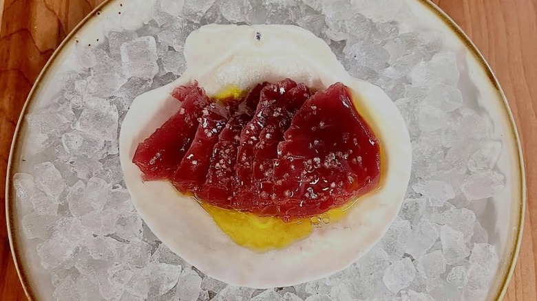 tuna crudo dish served on a half shell on top of a plate of ice