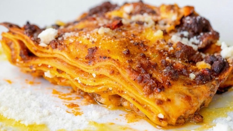 closeup of a piece of lasagna sprinkled with parmesan cheese and olive oil
