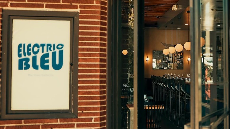 exterior of restaurant electric bleu with sign on brick wall and open door exposing the interior