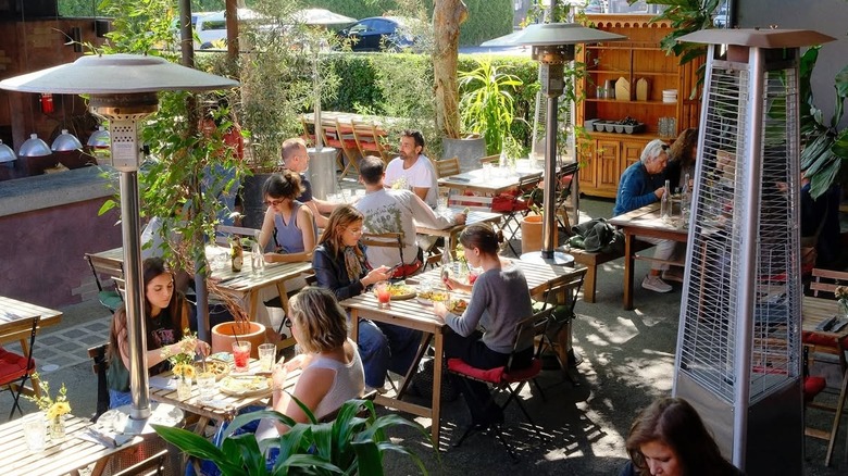 various people eating at an outdoor restaurant with wooden tables and foliage