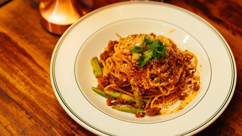 a plate of pasta in red sauce with vegetables on a wooden table