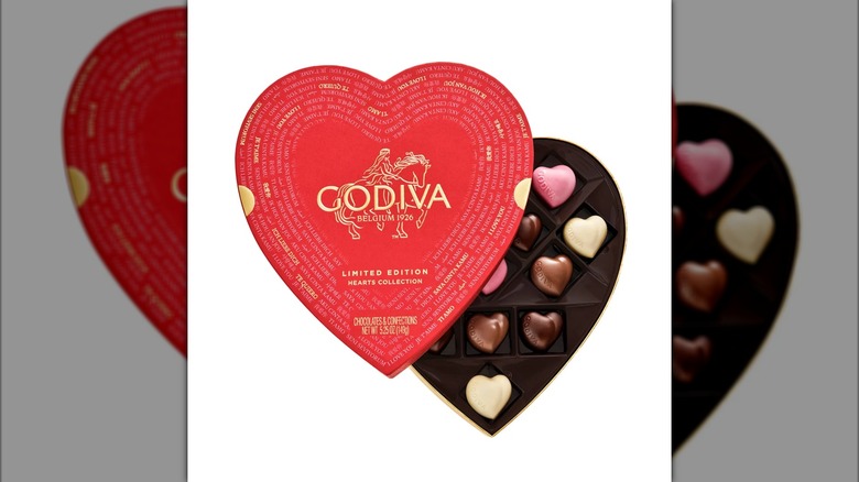 An open, heart-shaped box of Godiva chocolate hearts against a white background