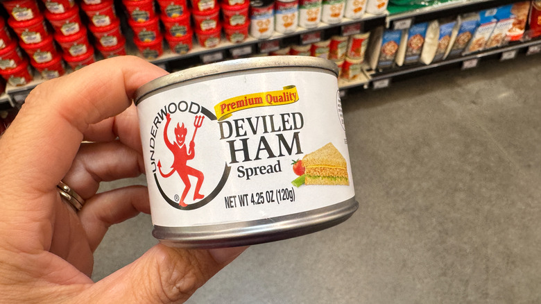 A hand holds up a can of Underwood Deviled Ham in a supermarket aisle