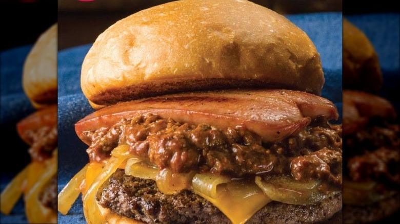 Closeup on a Fuddruckers burger with chili and a hot dog split open