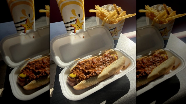 A Hardee's Jumbo Chili Dog in a white food container sits next to Hardee's fries and a fountain drink