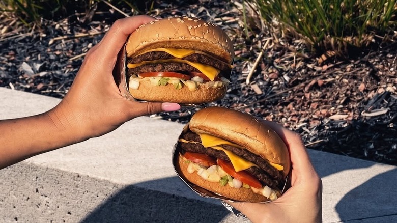 Hands hold up two Double Del Cheeseburgers from Del Taco