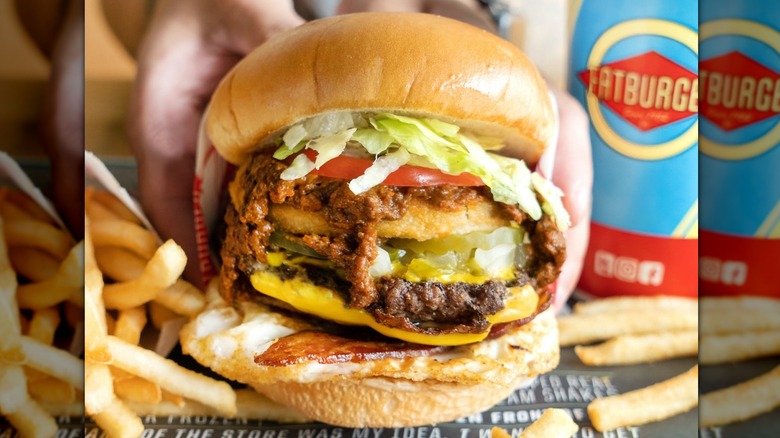 Hands hold a Fatburger with chili