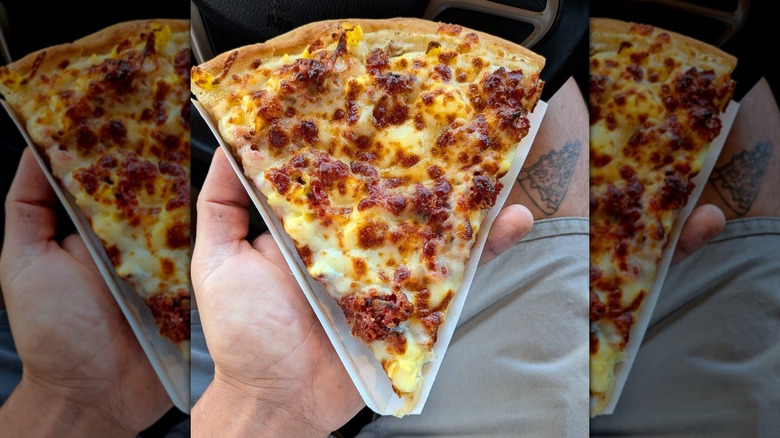 A hand holds up a slice of Bacon Breakfast Pizza from Casey's.
