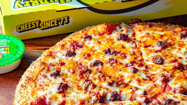 A Hungry Howie's Bacon Cheddar Cheeseburger Pizza sits next to a pizza box and a container of ranch dressing.